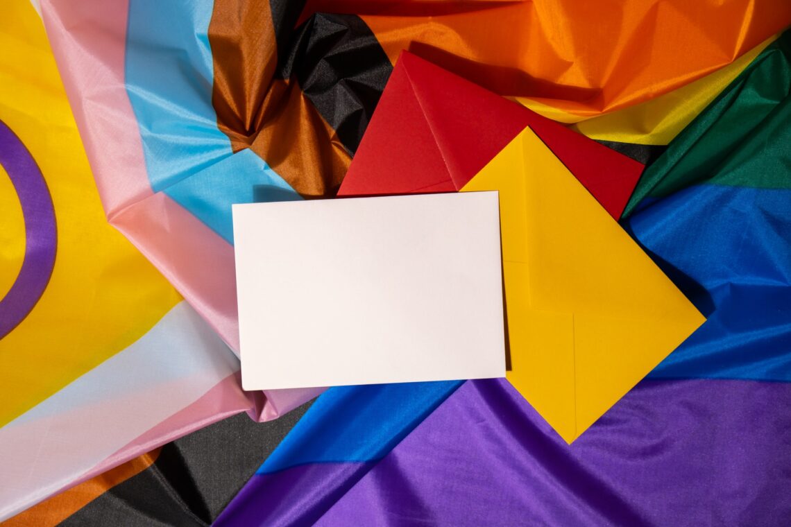 Empty paper blank on Rainbow LGBTQIA flag made from silk material. Mock up template copy space for