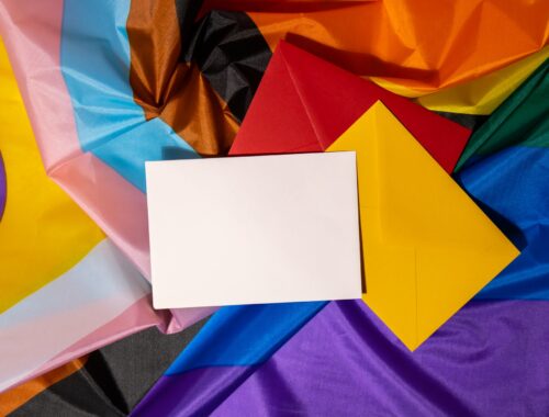 Empty paper blank on Rainbow LGBTQIA flag made from silk material. Mock up template copy space for