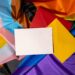 Empty paper blank on Rainbow LGBTQIA flag made from silk material. Mock up template copy space for